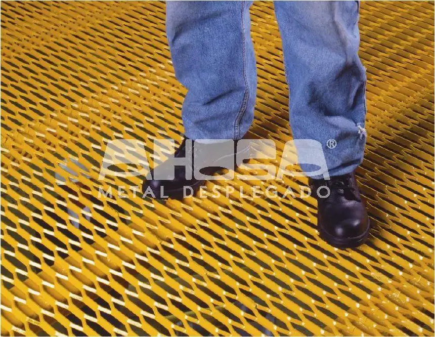 Persona con zapatos de seguridad parada sobre un piso de grating AHOSA pintado de amarillo, mostrando la superficie antideslizante del metal desplegado.